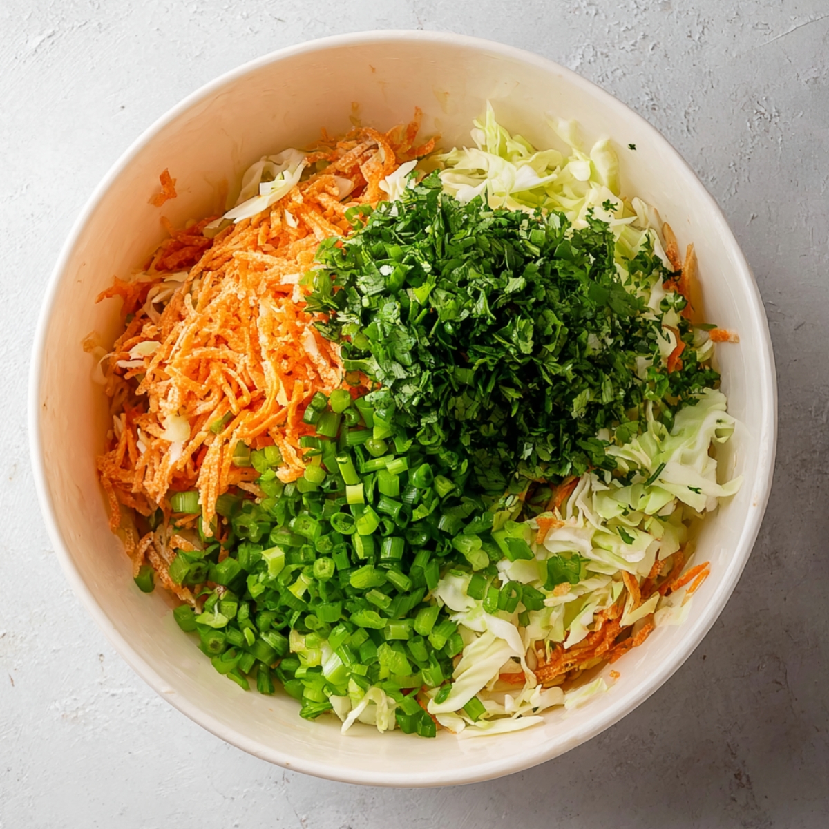 A bowl filled with shredded cabbage, grated carrots, chopped green onions, and fresh cilantro, ready to be mixed for a vibrant salad.